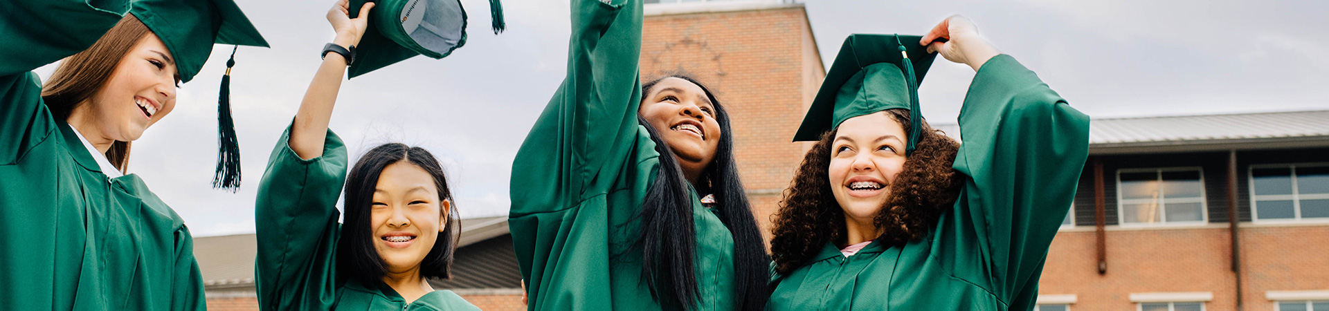  A group of teen girls wearing green graduation robes and tossing their caps in the air 