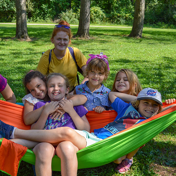 A group of smiling girls laying in an orange and green hammock