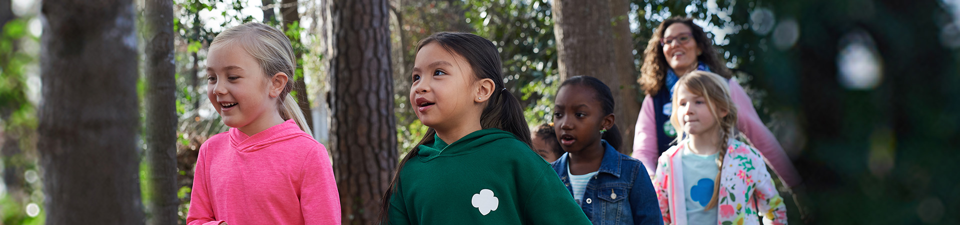  A young Girl Scout troop being led through the woods by an adult woman 