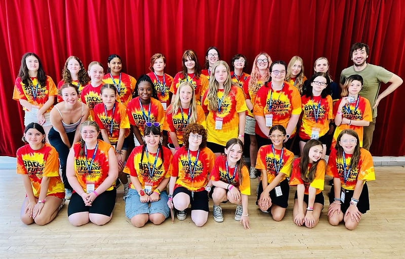 A group of teen girls all wearing blue tie dye shirts in a dance class with their arms up