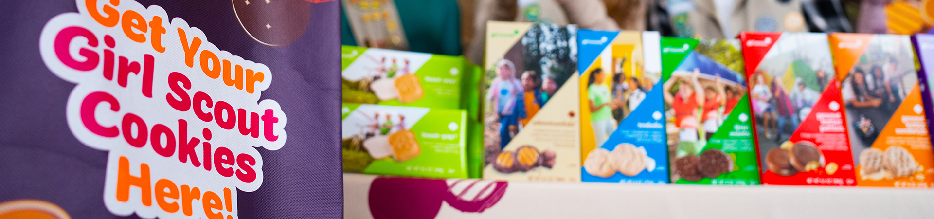  girl scout wearing uniform sash putting trefoil girl scout cookie boxes into cookie transport bag 