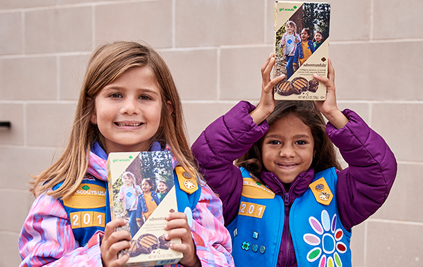 Two Daisies standing next to each other holding cookie boxes and smiling