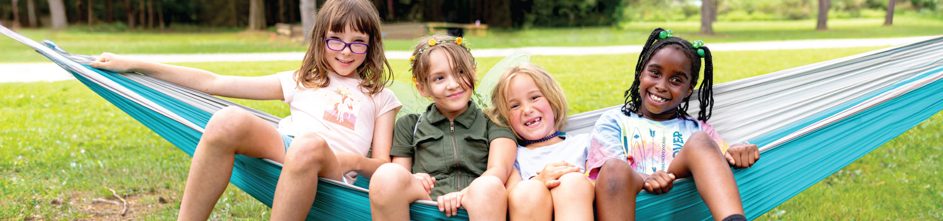  adult volunteer wearing vest with a girl scout junior (right, in baseball cap) and daisy (left) outside at a park smiling and looking at one another 