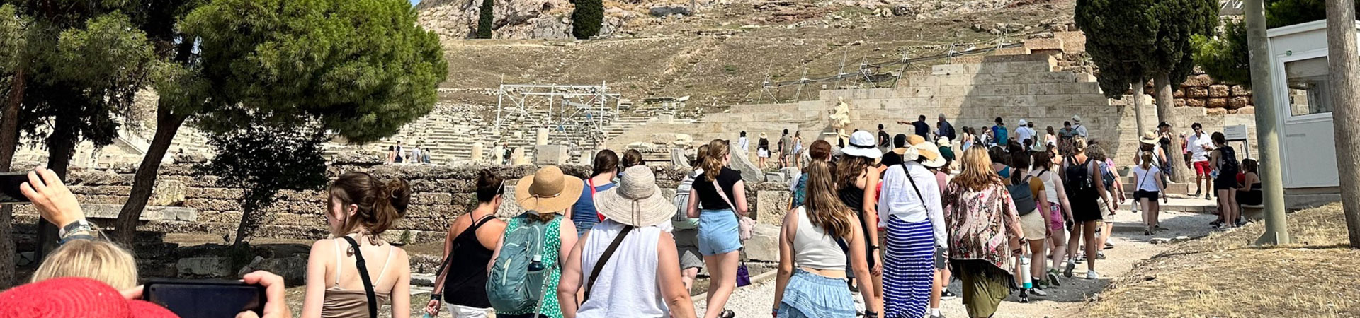  A large group of girls and women outside and dressed for warm weather. They are walking toward a large set of stone steps carved into a hill 