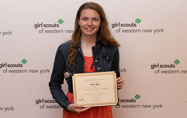 ambassador high school girl scout wearing sash outside against green background