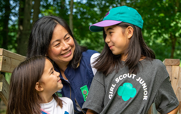 An adult woman, Junior Girl Scout, and Daisy Girl Scout all looking at each other andd laughing